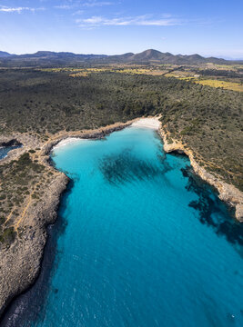Aerial view of Cala Varques with turquoise water, rocky cliffs, and Mediterranean vegetation in Mallorca, Spain.