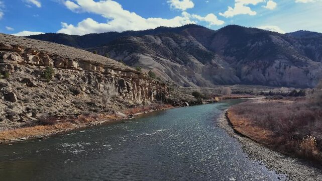 Aerial view of a river flowing through a valley with rocky cliffs and mountains under a blue sky in Gypsum, Colorado, United States.