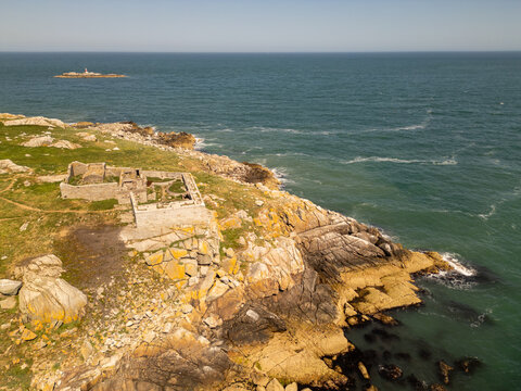Aerial view of the historic stone ruins on Dalkey Island, surrounded by rugged rocky coastline, green grass, and the blue waters of the Irish Sea near Dublin, County Dublin, Ireland.