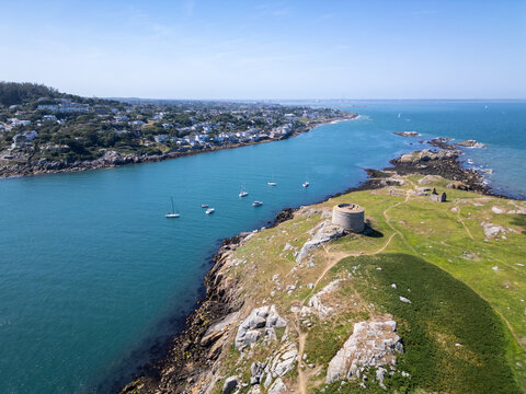 Aerial view of Dalkey Island featuring its historic Martello tower, rocky coastline, and surrounding blue waters with small boats in the bay, Dublin, County Dublin, Ireland.