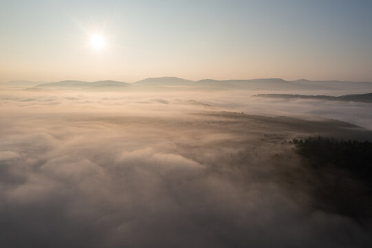 Aerial view of a landscape covered in thick morning fog with rolling hills in the background under a bright sun in Weidenthal, Rhineland-Palatinate, Germany.