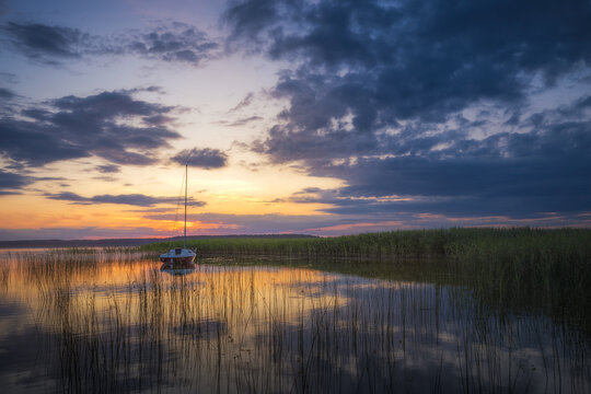 View of Lake Lasmiady with a sailboat moored among reeds at sunset under a dramatic cloudy sky in Elk, Warminsko-Mazurskie, Poland.