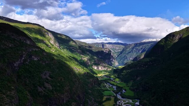 Aerial view of the lush Flam valley with steep mountains, a winding river, and green meadows in Flam, Vestland, Norway.