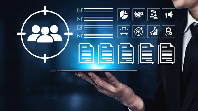 A businessman holds a tablet showcasing various analytics and target audience visuals, symbolizing data-driven decision-making in a modern corporate landscape. Ledger