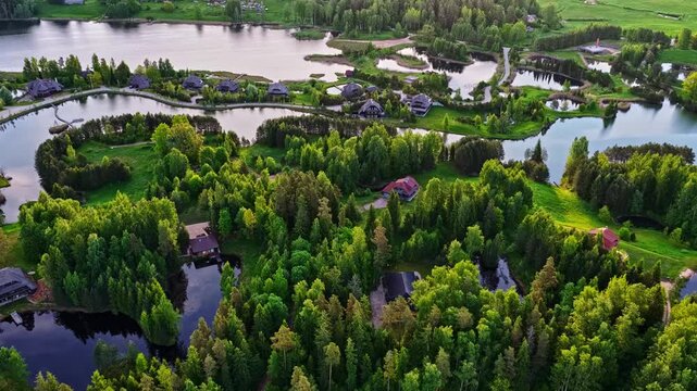 Aerial view of Amatciems village with wooden houses nestled among lush green forests and serene ponds in Amatciems, Cesu novads, Latvia.