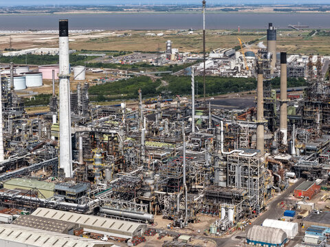Aerial view of an industrial oil refinery with tall chimneys, complex piping systems, and storage tanks located in the United Kingdom.