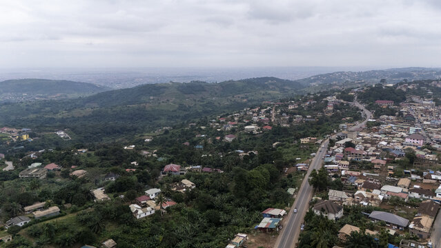 Aerial view of the town of Aburi nestled in the lush hills, featuring residential buildings, winding roads, and dense tropical vegetation under a cloudy sky in Aburi, Eastern Region, Ghana.