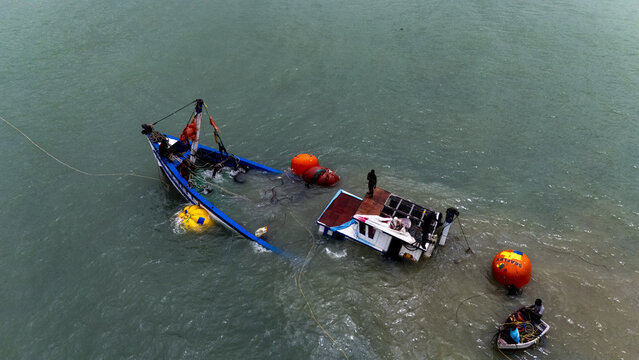 Aerial view of a partially submerged fishing boat with fishermen working on deck and orange buoys in the water near Cape Coast, Central Region, Ghana.