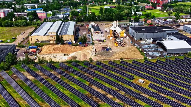 Aerial view of a large solar farm with rows of photovoltaic panels, industrial buildings, and construction materials in Jelgava, Jelgava pilseta, Latvia.
