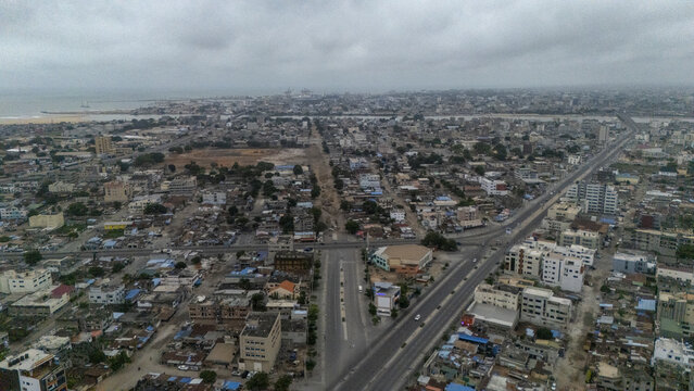 Aerial view of the urban landscape of Cotonou, featuring dense residential and commercial buildings, wide roads, and the coastline under a cloudy sky in Cotonou, Littoral Department, Benin.