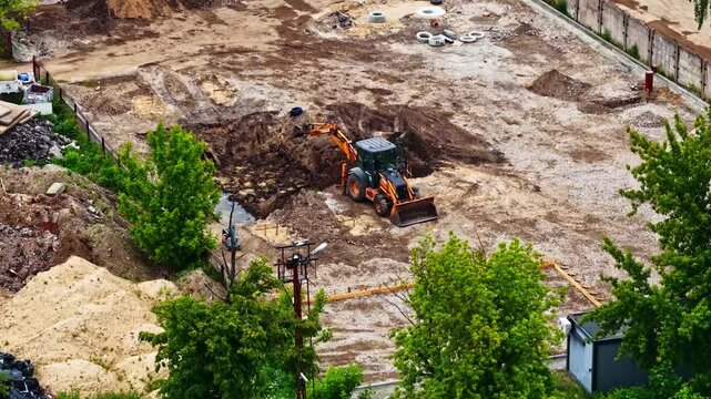 Aerial view of an orange backhoe loader digging at a construction site near Jelgava Palace in Jelgava, Jelgava pilseta, Latvia.