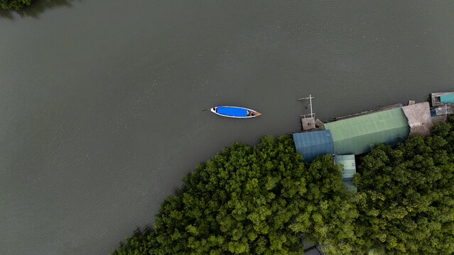 Aerial view of a small boat with a blue canopy floating on the river near the Gogotinkpon stilt village surrounded by lush mangrove vegetation in Kpomasse, Mono, Benin.