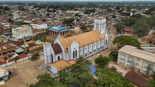 Aerial view of the Basilica of the Immaculate Conception surrounded by urban rooftops and lush trees in Ouidah, Atlantique, Benin.