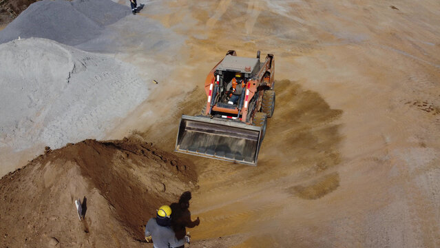 Aerial view of a skid steer loader operating in a mining site with piles of gravel and sand and workers in safety gear in Barranca, Lima Region, Peru.