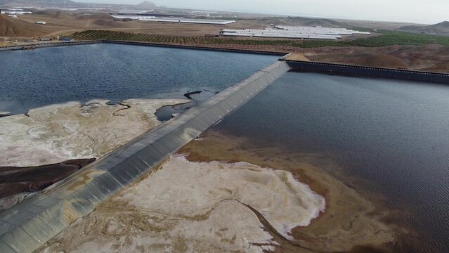 Aerial view of the Relave Minero tailings pond featuring large water reservoirs with sediment deposits in the arid desert landscape of Barranca, Lima Region, Peru.