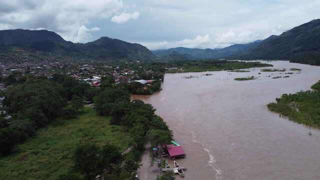 Aerial view of Pichanaki town along the Perene River with lush vegetation, surrounding mountains, and small boats moored at the riverbank in Pichanaki, Junin, Peru.