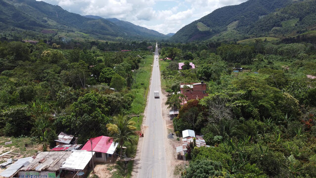 Aerial view of a long straight road stretching through the lush green valley of Pichanaki, surrounded by dense tropical vegetation and small houses in Pichanaki, Junin, Peru.