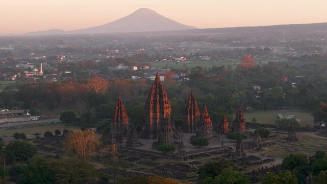 Aerial view of the historic Prambanan Temple complex illuminated by golden hour light with a mountain in the background in Kecamatan Prambanan, Daerah Istimewa Yogya, Indonesia.