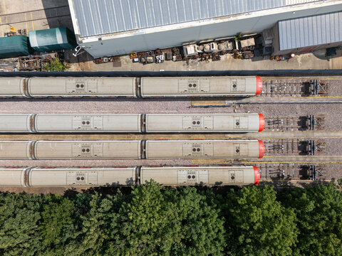 Aerial view of Ealing Common Depot with multiple London Underground tube trains parked on parallel tracks next to a depot building and lush green trees in London, England, United Kingdom.