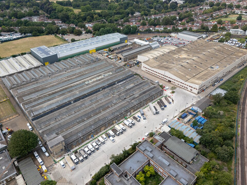 London, United Kingdom - 10 July 2026: Aerial view of Acton Works featuring industrial warehouses with sawtooth roofs, a parking area with trucks and vans, and urban greenery.
