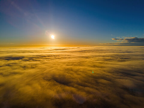 Aerial view of a golden sunset over a vast sea of clouds covering the landscape in Vidzeme, Latvia.