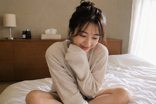 ベッドにあぐらで座るベージュニットの女性