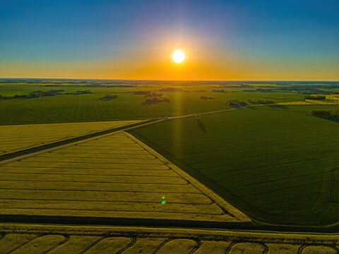 Aerial view of agricultural fields at sunset with warm golden light illuminating the landscape in Jelgava, Latvia.