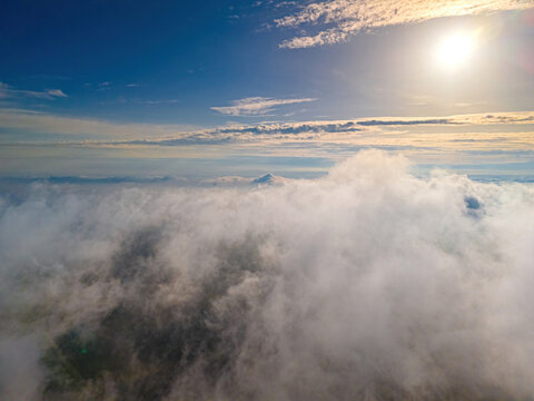 Aerial view of thick white clouds illuminated by the bright sun in the blue sky over the landscape of Vidzeme, Latvia.