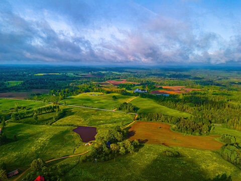 Aerial view of rolling green hills, agricultural fields, small ponds, and patches of forest in the Vidzeme region of Latvia.