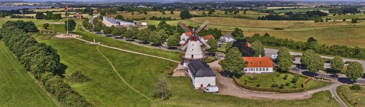 Sonderborg, Syddanmark, Denmark - 08 July 2026: Aerial view of the historic Dybbol Mill surrounded by lush green fields, trees, and traditional buildings under a clear summer sky.