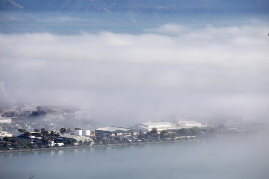 Nelson, New Zealand - 14 July 2026: View of Port Nelson partially obscured by thick morning fog with industrial buildings and calm waterfront visible.