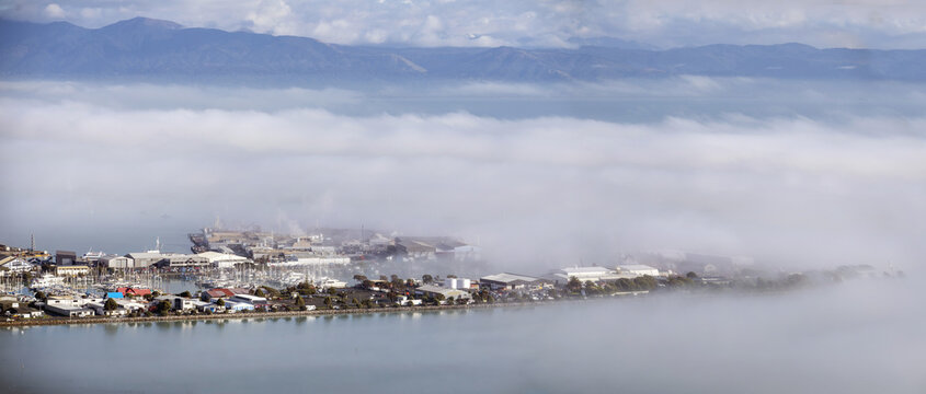 Nelson, Nelson Region, New Zealand - 14 July 2026: View of Port Nelson partially obscured by low-lying fog with industrial buildings and boats in the harbor.