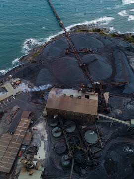 Aerial view of the iron ore pelletizing plant with large stockpiles of iron ore, industrial machinery, and a long conveyor belt extending into the ocean in Port Latta, Tasmania, Australia.