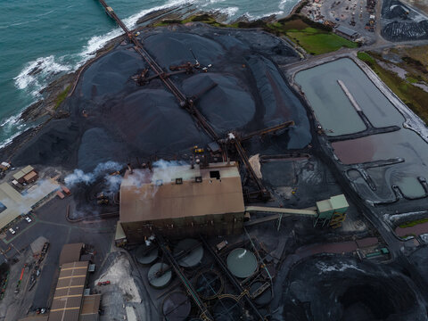 Aerial view of the iron ore pelletizing plant with large stockpiles, conveyor systems, industrial buildings, and settling ponds along the rugged coastline in Port Latta, Tasmania, Australia.