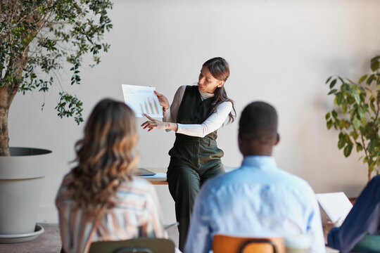 Female presenter discussing business growth charts during a corporate meeting, explaining market trends and financial analytics to a diverse team in a modern office