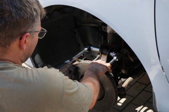 Mechanic replacing a suspension strut with hand tools. Automotive repair, DIY vehicle maintenance, shock absorber replacement, brake service and professional garage work.