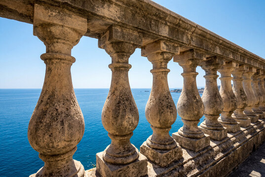 Weathered stone balustrade overlooking a vast blue ocean and clear sky