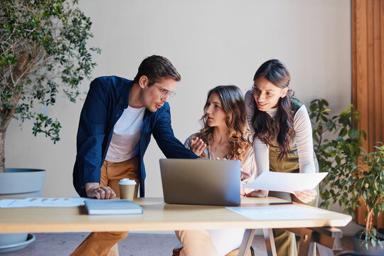 Three diverse young professionals actively collaborating around a laptop and documents