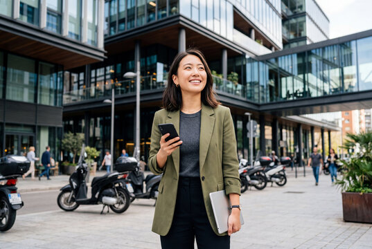 Asian businesswoman walking in city with laptop and phone