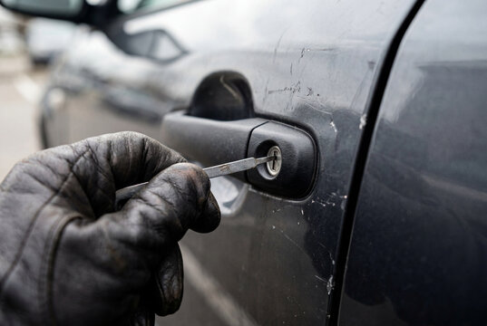 Thief in black leather glove unlocking car door with tool