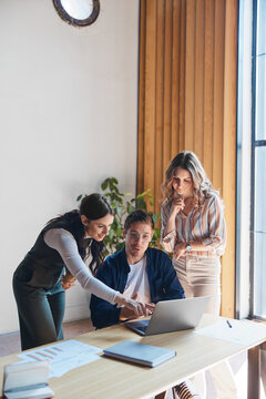 Diverse business professionals actively collaborating around a laptop. A female colleague pointing at the screen during a focused discussion