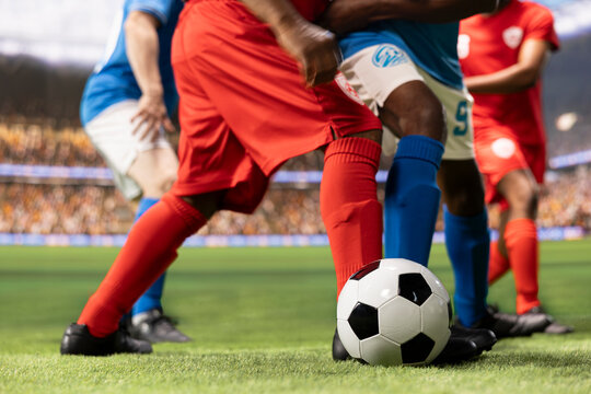Low-angle view shows soccer players in red and blue kits competing for ball possession in an intense duel, emphasizing dribbling and attacking footwork.