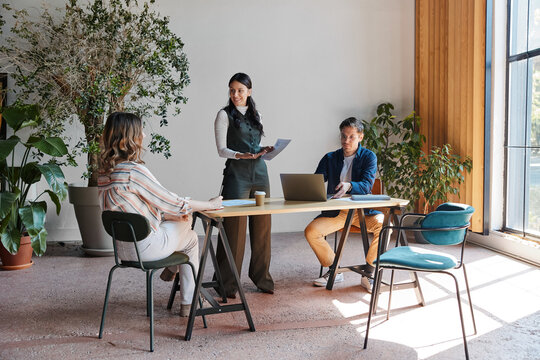 Diverse business team collaborating during an informal office meeting, discussing project details and ideas, fostering professional development and teamwork in a modern workspace
