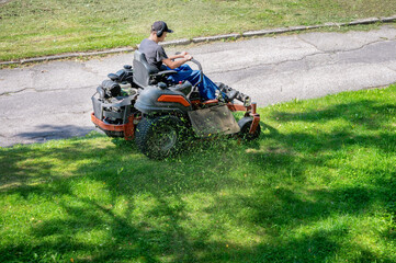 Man riding professional zero turn lawn mower machine cutting green grass in park. Gardener operating riding lawnmower for lawn care maintenance. No faces © Gereish