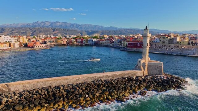 Aerial view of the historic Old Venetian Port of Chania featuring the iconic lighthouse, stone breakwater, colorful waterfront buildings, and calm harbor waters in Chania, Greece.