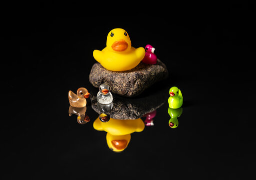 Cute yellow rubber duck surrounded by different colored mini toy ducks on a black background