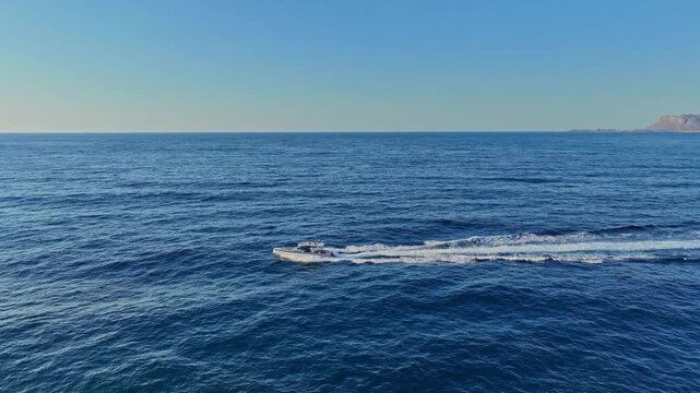 Aerial view of a small motorboat leaving a white wake as it travels across the deep blue Mediterranean Sea near Chania, Greece.