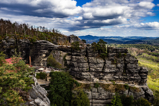View of Pravcicka brana, a natural sandstone arch formation surrounded by forest and rugged rock formations under a cloudy sky, Hrensko, Usti nad Labem Region, Czechia.