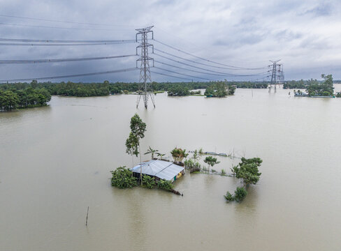 Banshkhali Upazila, Bangladesh - 11 July 2026: Aerial view of a house isolated by floodwaters with electricity pylons standing in the submerged landscape under a cloudy sky.