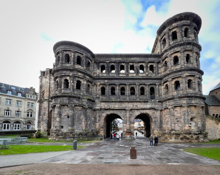 View of the historic Roman city gate Porta Nigra with its weathered stone facade, arched gateways, and people walking in the square in Trier, Rheinland-Pfalz, Germany.